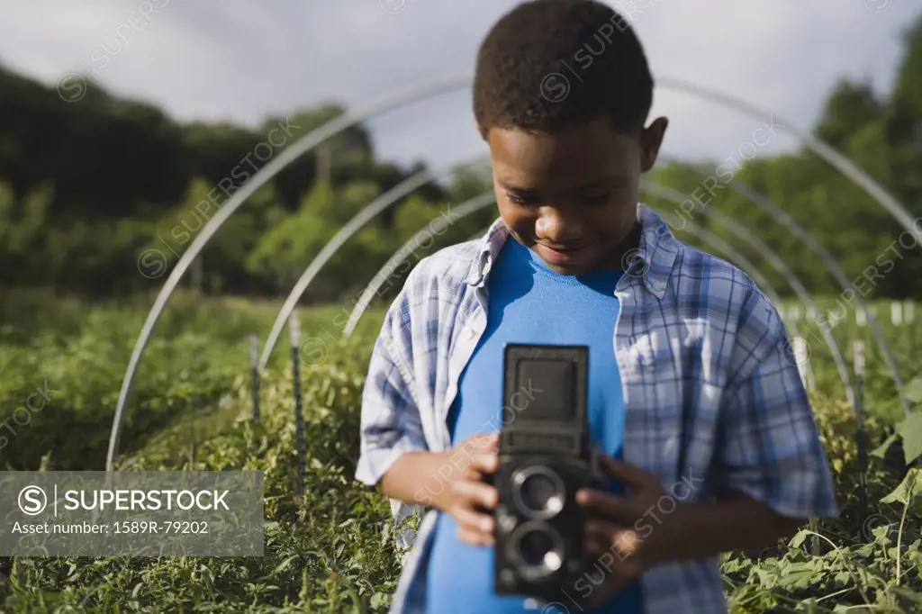African boy holding retro camera in garden