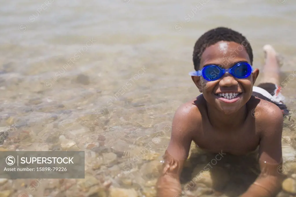 African boy wearing goggles and laying in shallow lake