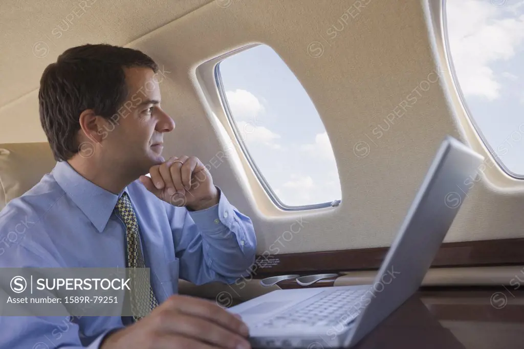Hispanic businessman with laptop looking out airplane window