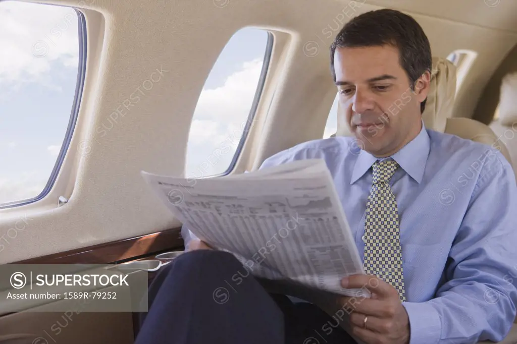 Hispanic businessman reading newspaper on airplane