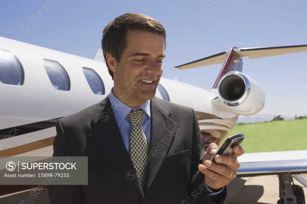 Hispanic businessman text messaging next to private jet