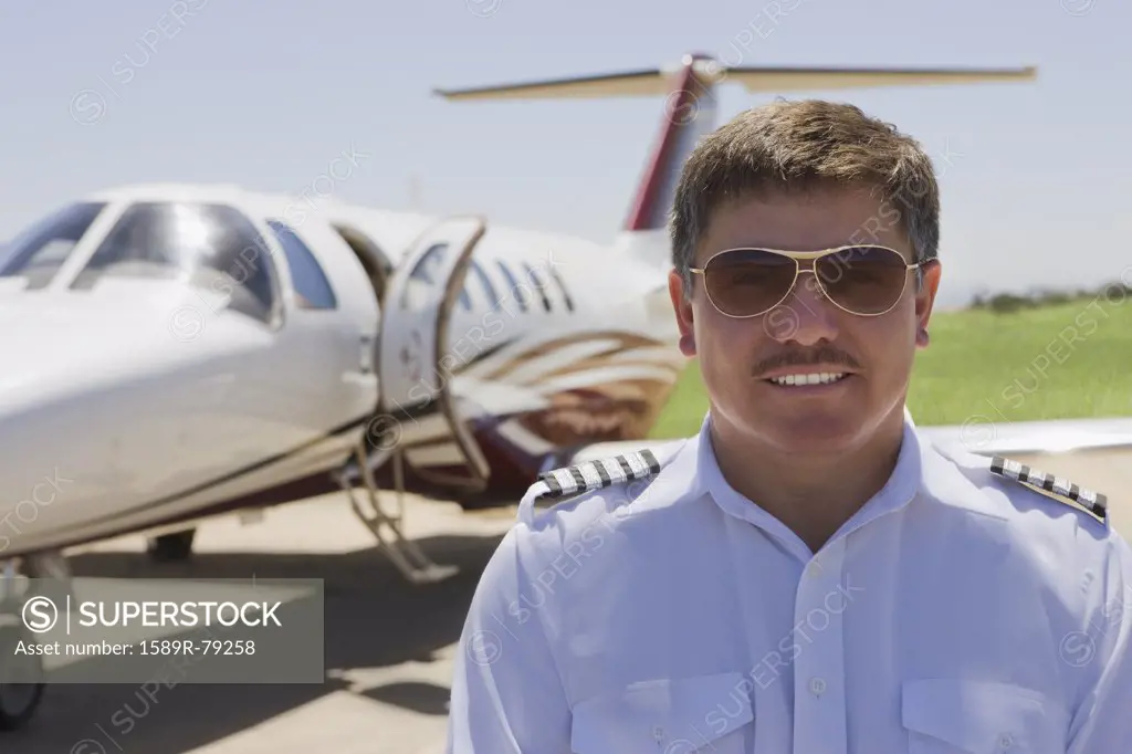 Hispanic pilot standing outside private jet