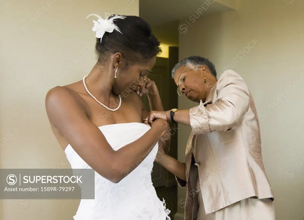 African mother helping bride with wedding dress
