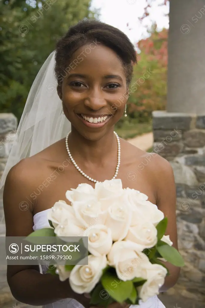 African bride holding rose bouquet and smiling