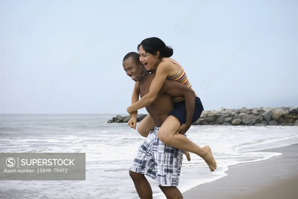 African man giving girlfriend piggy back ride at beach