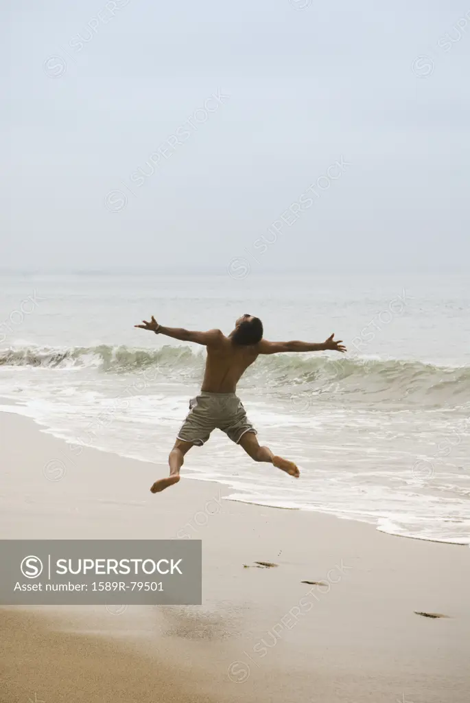 Mixed race man jumping in air on beach