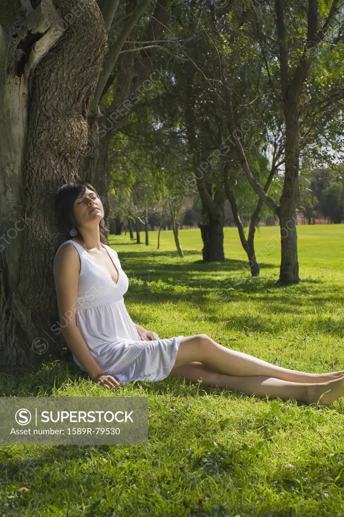 Hispanic woman relaxing against tree in park