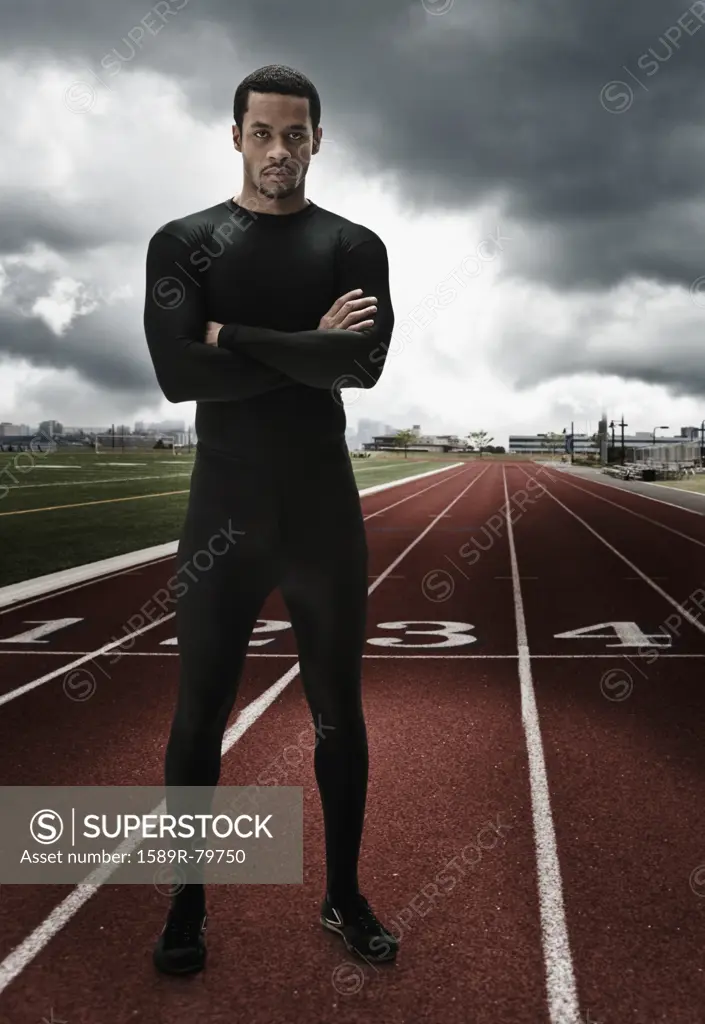 Serious mixed race athlete with arms crossed on running track