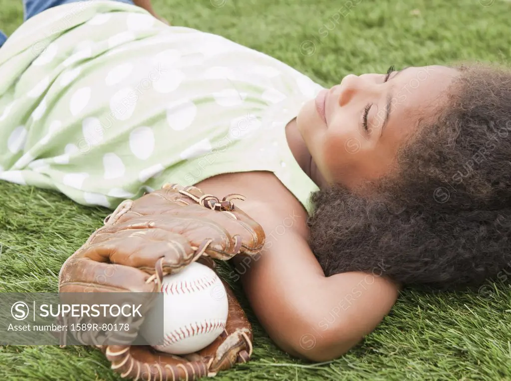 Mixed race girl laying next to baseball glove and ball