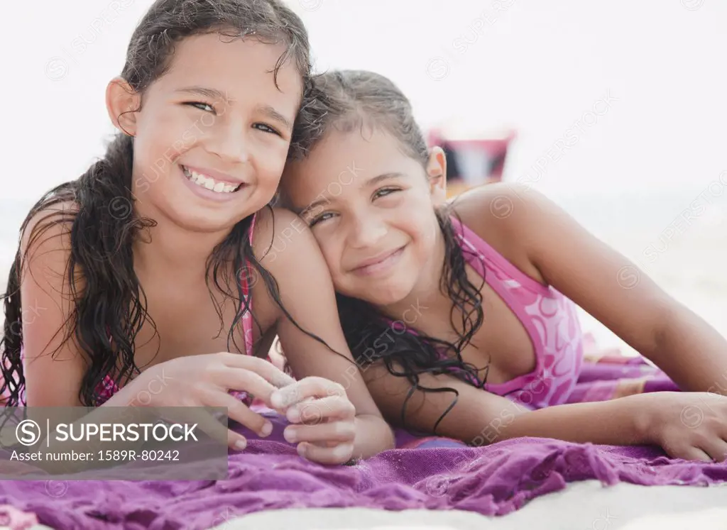 Hispanic sisters relaxing on towel at beach