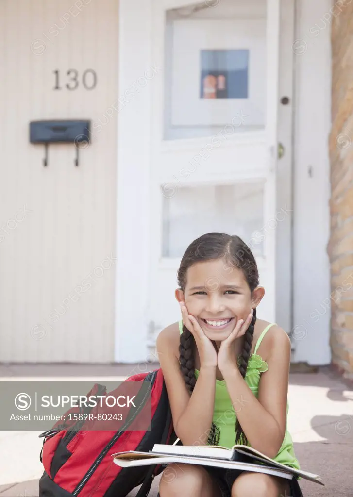 Hispanic girl sitting with school books on front stoop