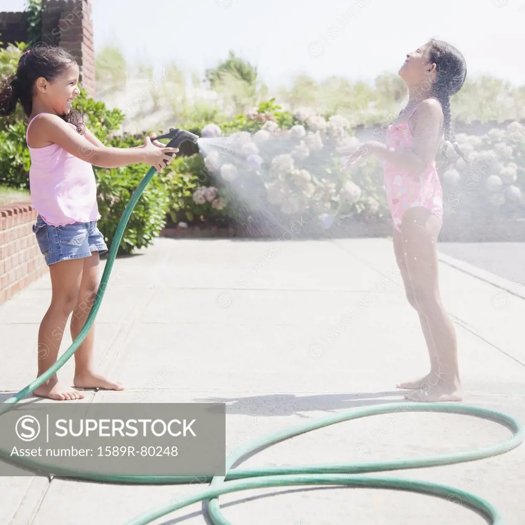 Hispanic girl spraying sister with hose