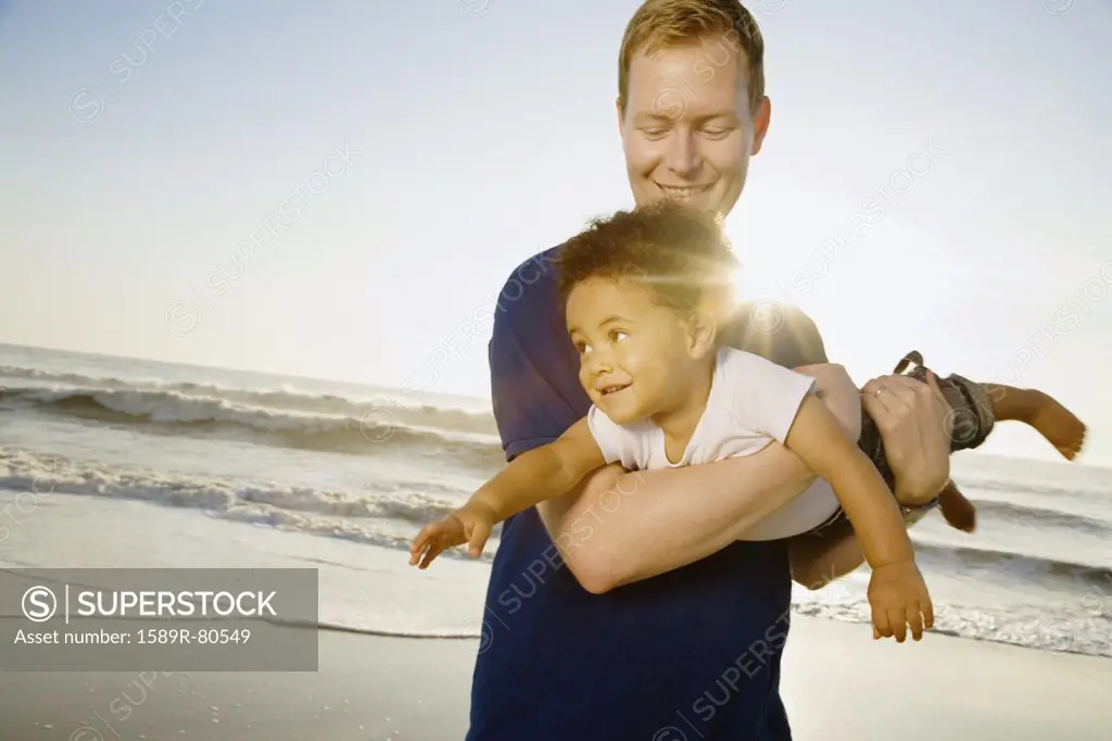 Father playing with mixed race son at beach