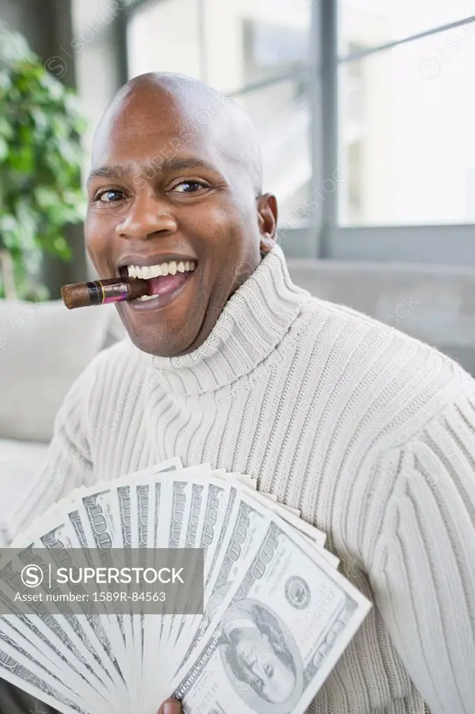 African man smoking cigar and holding 100 dollar bills