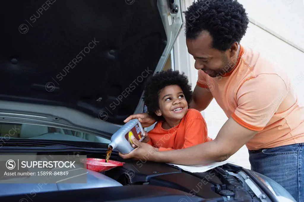 African father helping son pour oil into car engine