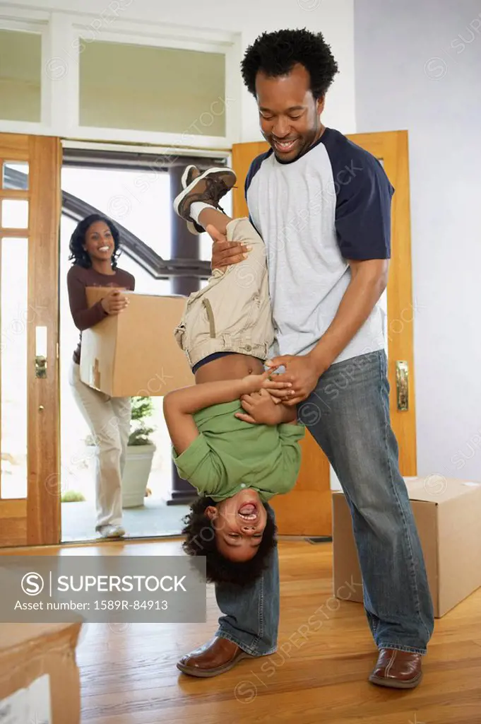 African father holding son upside down in new home