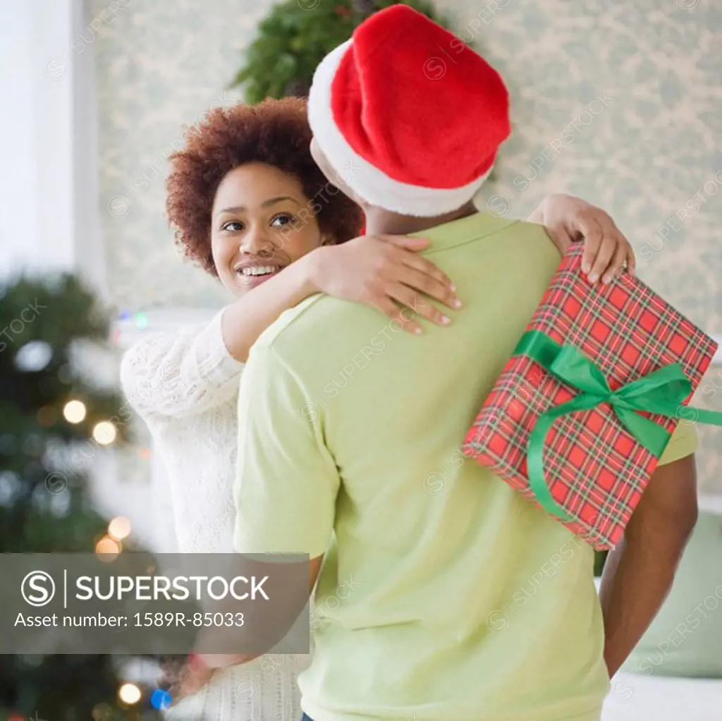 Mixed race woman hugging boyfriend and holding Christmas present