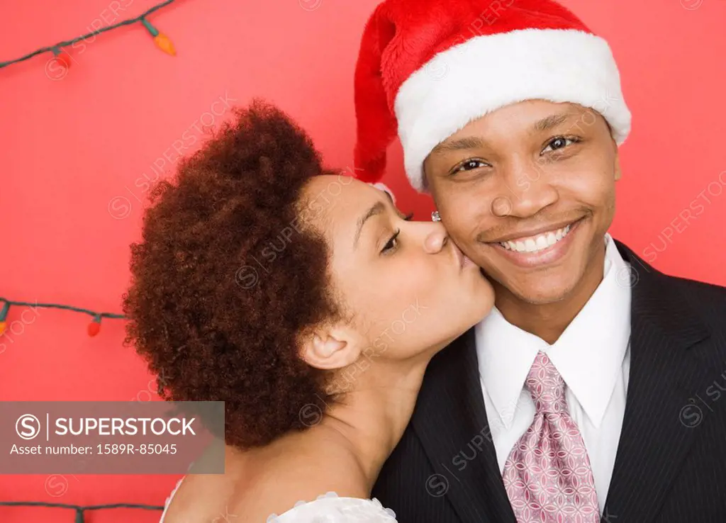 Mixed race woman kissing boyfriend in santa hat