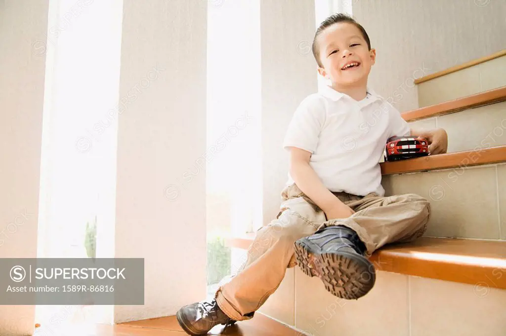 Hispanic boy sitting on staircase with toy car
