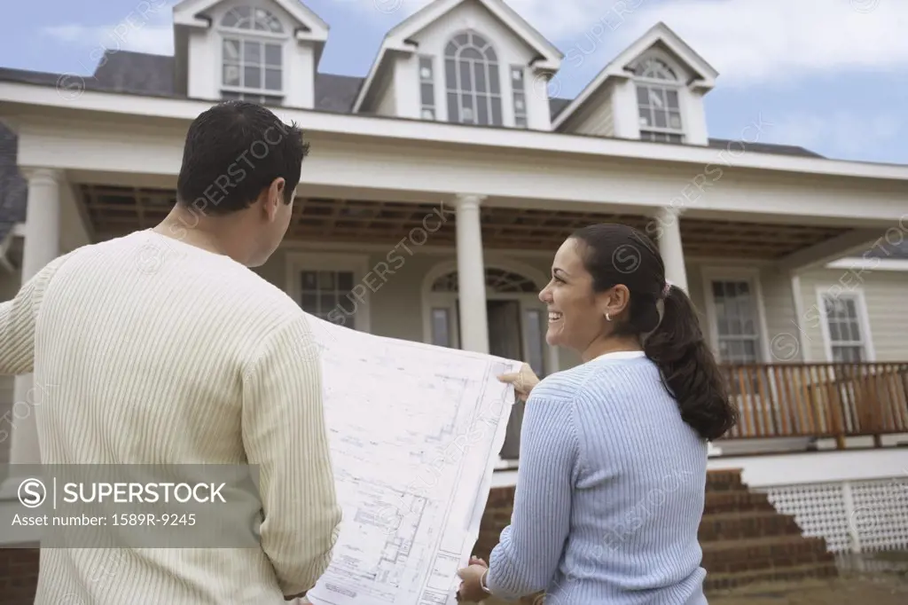 Rear view of couple looking at house plans outside front of house