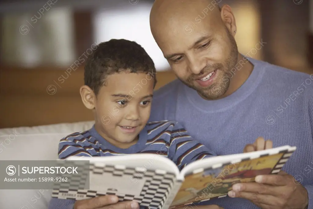 Father and son reading book while sitting on couch