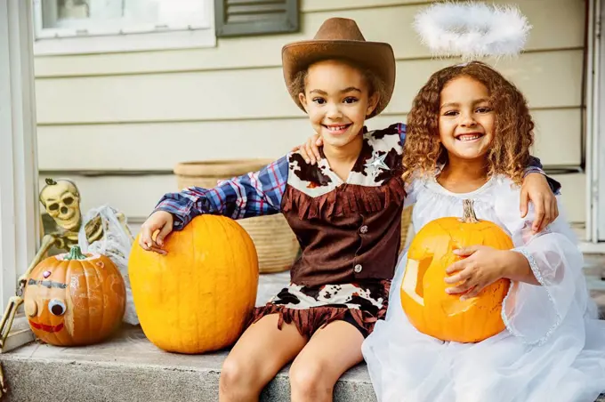 Sisters wearing Halloween costumes with jack-o-lanterns on porch