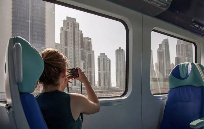 Caucasian woman photographing Dubai cityscape on train, Dubai Emirate, United Arab Emirates