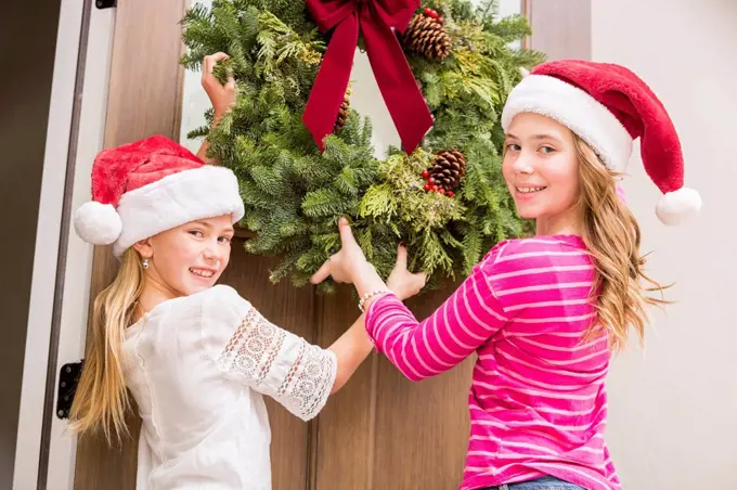 Caucasian girls hanging Christmas wreath