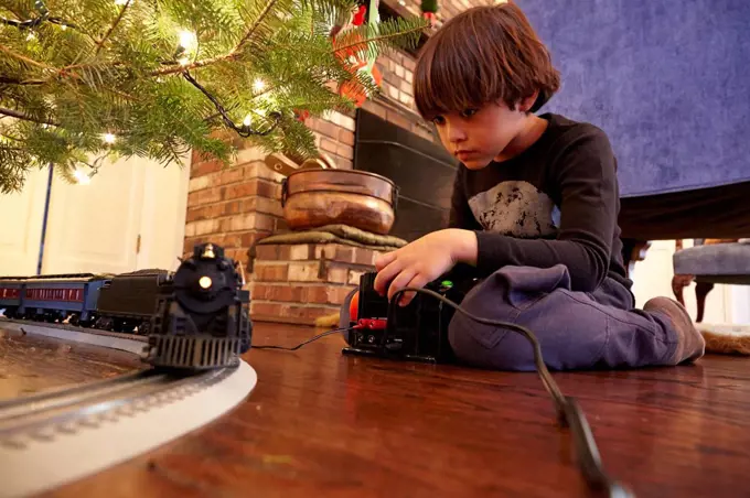 Mixed race boy playing with train under Christmas tree