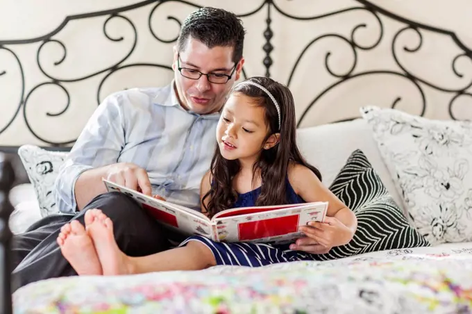 Father reading to daughter on bed