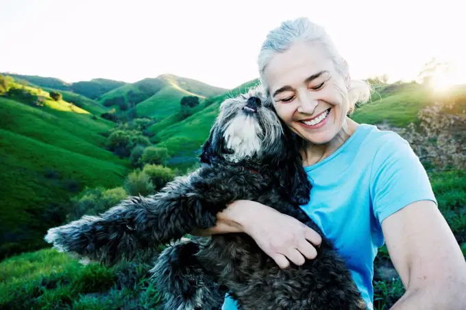 Older Caucasian woman hugging dog on rural hilltop