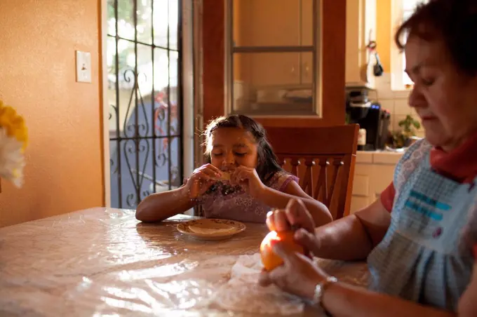 Hispanic grandmother and granddaughter eating in kitchen