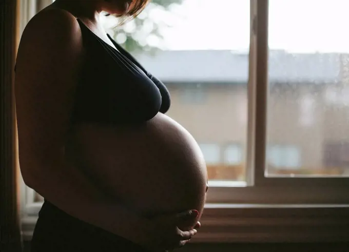 Pregnant Caucasian woman standing at window