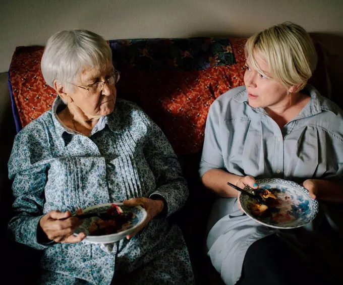 Older woman and granddaughter eating on sofa