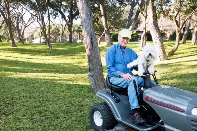 Older Caucasian man on riding lawnmower with pet dog
