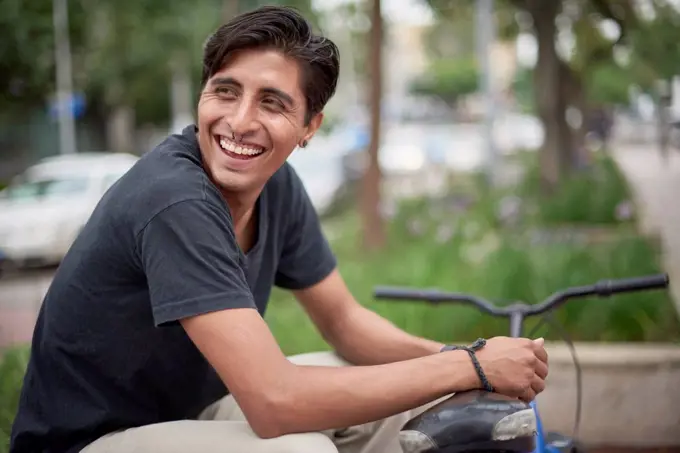 Laughing Hispanic man sitting with bicycle