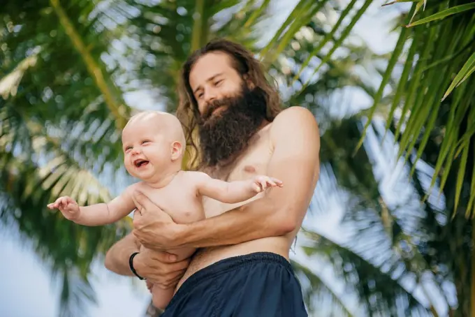 Caucasian father holding baby daughter under palm tree