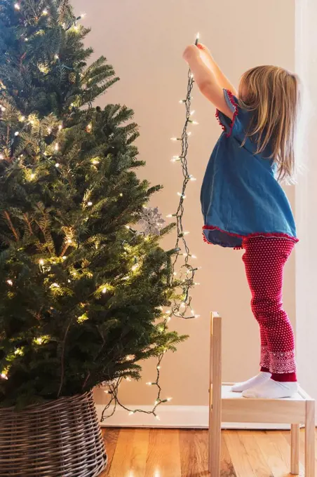 Caucasian girl hanging lights on Christmas tree