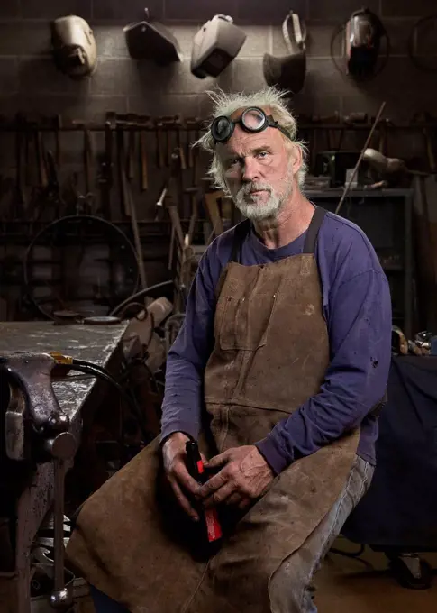 Portrait of serious Caucasian blacksmith in workshop drinking beer