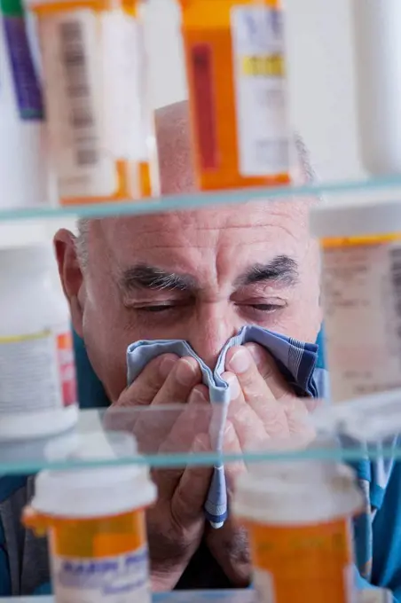 Hispanic man wiping nose near medicine cabinet