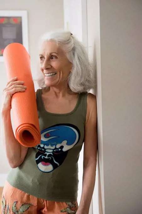 Older woman leaning on wall holding exercise mat