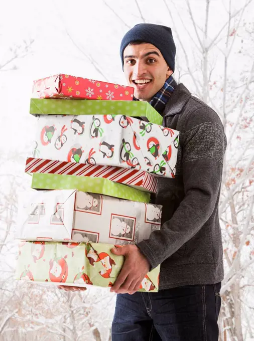 Hispanic man holding Christmas gifts in snow