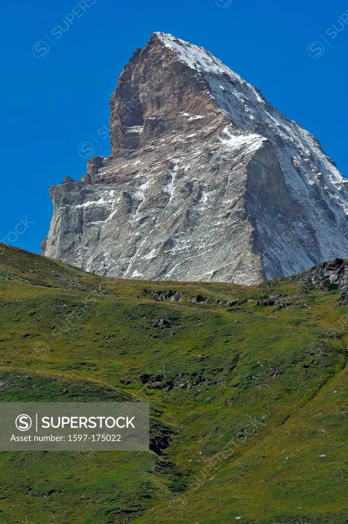 the imperious Matterhorn in the swiss alps above Zermatt. In the foreground summer grass on the hills