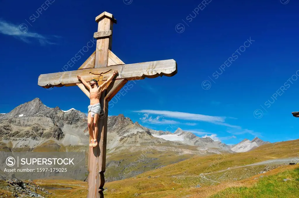 Cross with jesus christ crucified, in the mountains, above a lake, with high alps in the distance, on a clear blue day