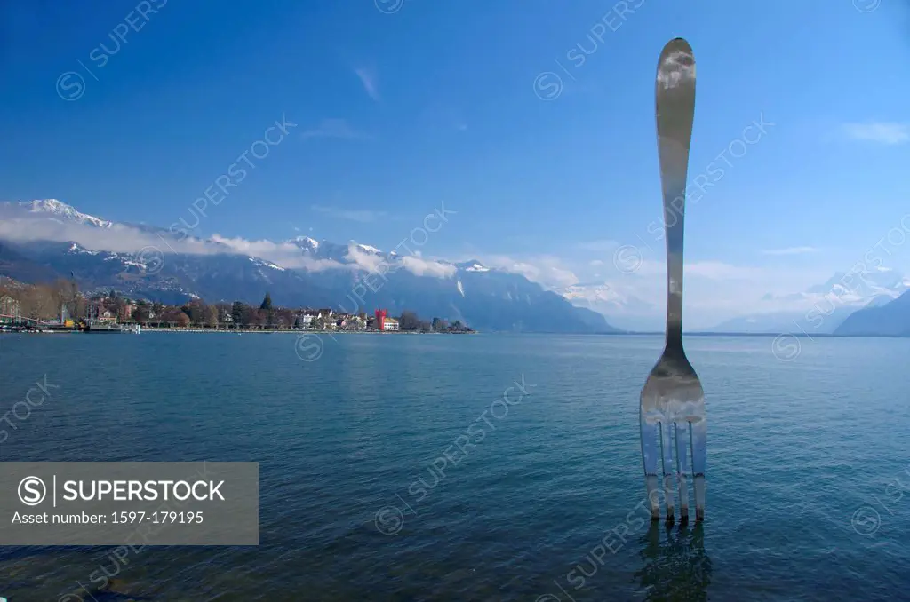 Giant fork sculpture inserted into lake Geneva Switzerland. In the background the town of Montreux and the bernese alps