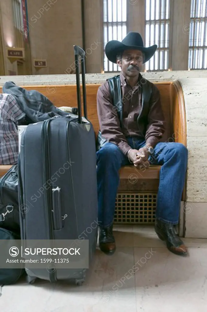 Black man with bags, cowboy hat and cowboy shoes waiting for train at 30th Street Station, AMTRAK Train Station in Philadelphia, PA