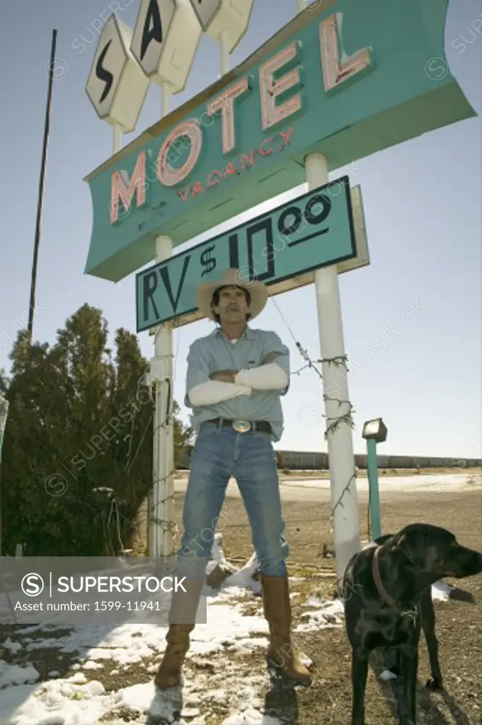 Cowboy with dog stand in front of Sands Motel sign with RV Parking for $10, located at the intersection of Route 54 & 380 in Carrizozo, New Mexico