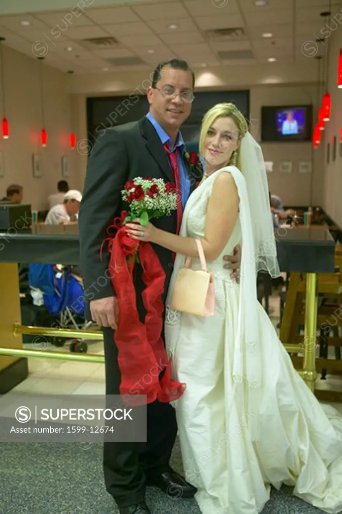Groom and Bride in wedding dress pose for picture in airport while on their way to honeymoon
