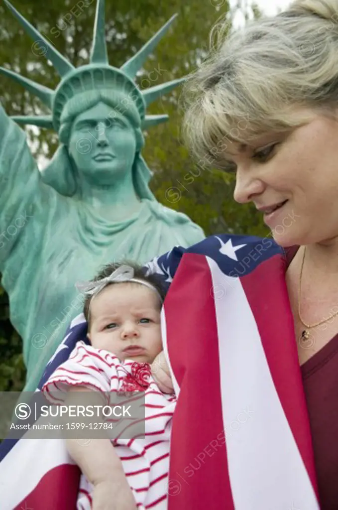 Mother and newborn baby (Sophia Larson) wrapped in American flag stand in front of a Statue of Liberty, was born on October 16th, the birthday of the 300 Millionth American, Ventura, California