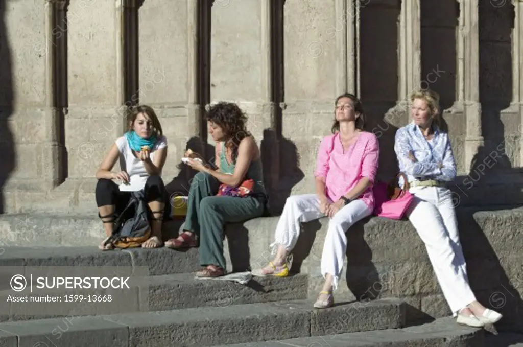 Four women relax in sunlight of old Barcelona in Barri Gotic area, the Gothic Quarter, Spain